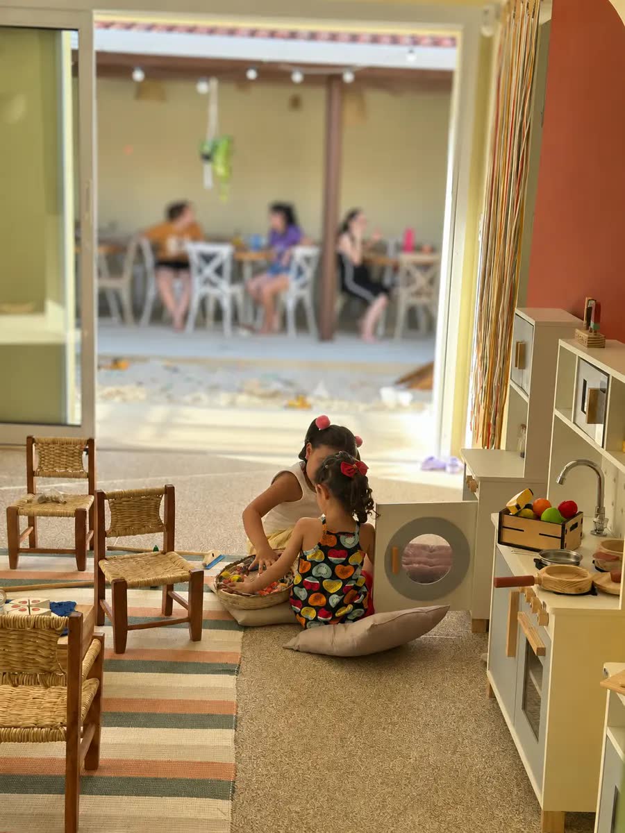 Pais e responsáveis na cafeteria do Di Maria enquanto as crianças brincam por perto.